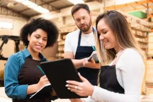 3 people look at a clipboard in a warehouse