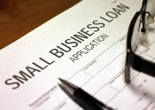 small businesses financial challenges Small business loan application form with pen and glasses on wooden desk.