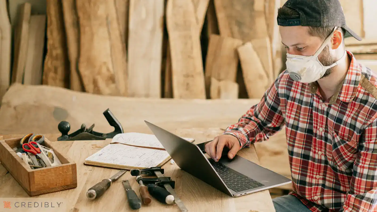 Man working on business debt schedule on laptop in workshop setting.