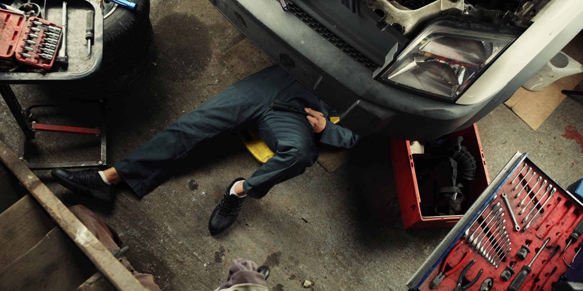 Auto repair technician inspecting car underside for repairs.