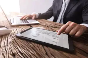 Business owner reviewing an invoice on a tablet while working on a laptop