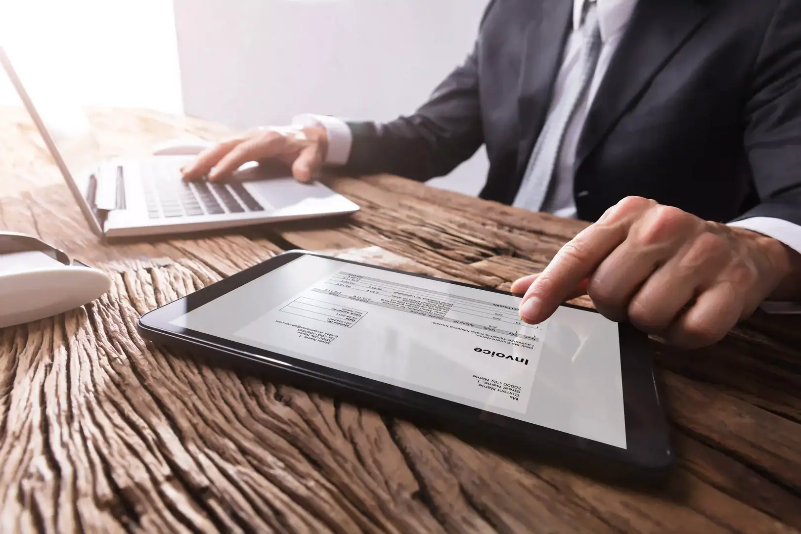 Business owner reviewing an invoice on a tablet while working on a laptop