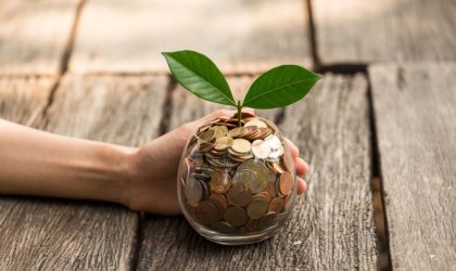 Small plant growing from coins in a glass jar, symbolizing financial growth and investment.