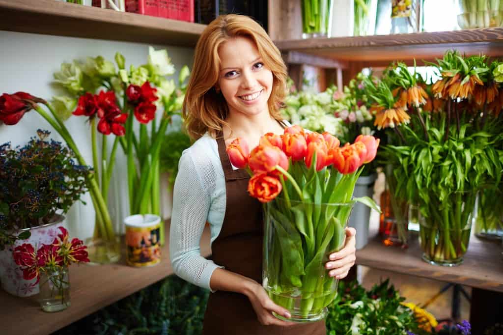 Smiling florist holding a vibrant bouquet of tulips in a flower shop.