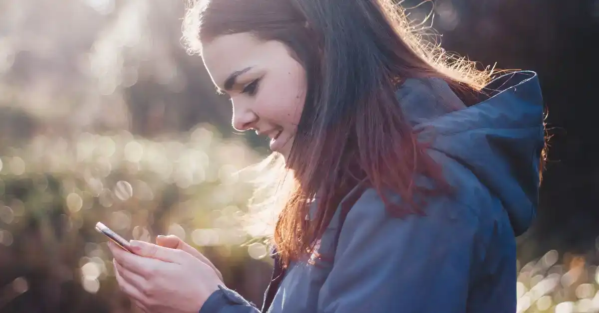 Young woman using her phone outdoors, representing small business loan needs.