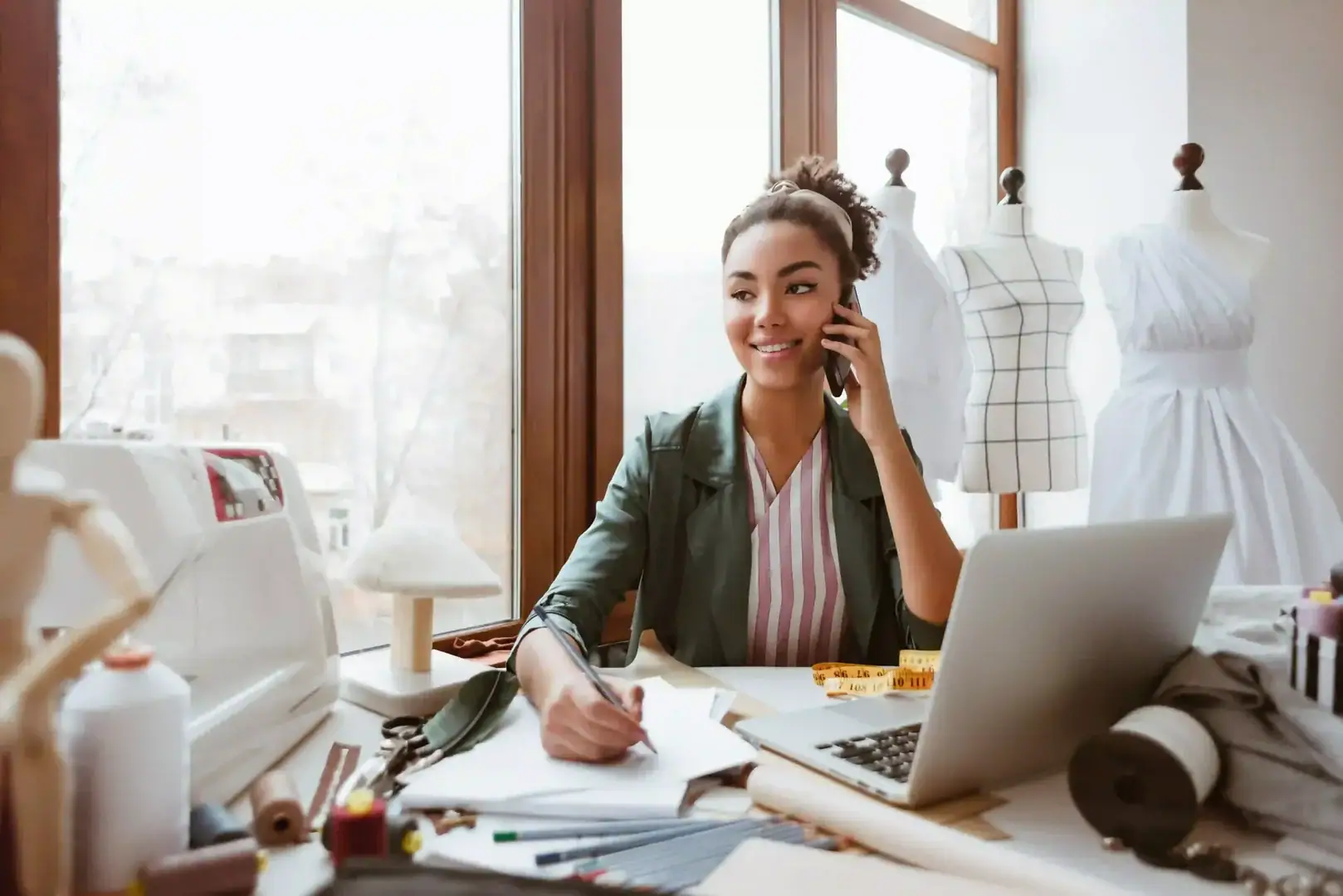 Small business owner working at a laptop and speaking on the phone in a clothing studio